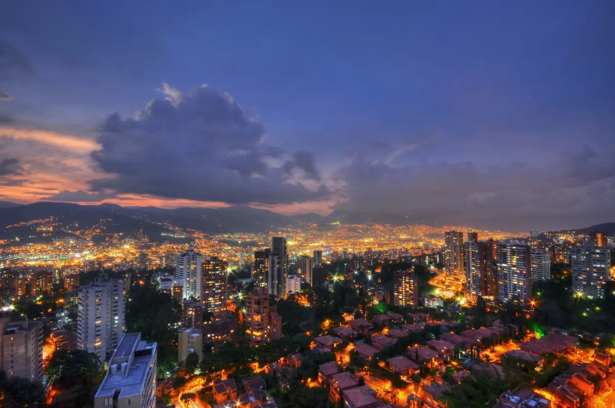 Medellin lit up at night in its valley, with mountains under the evening clouds.