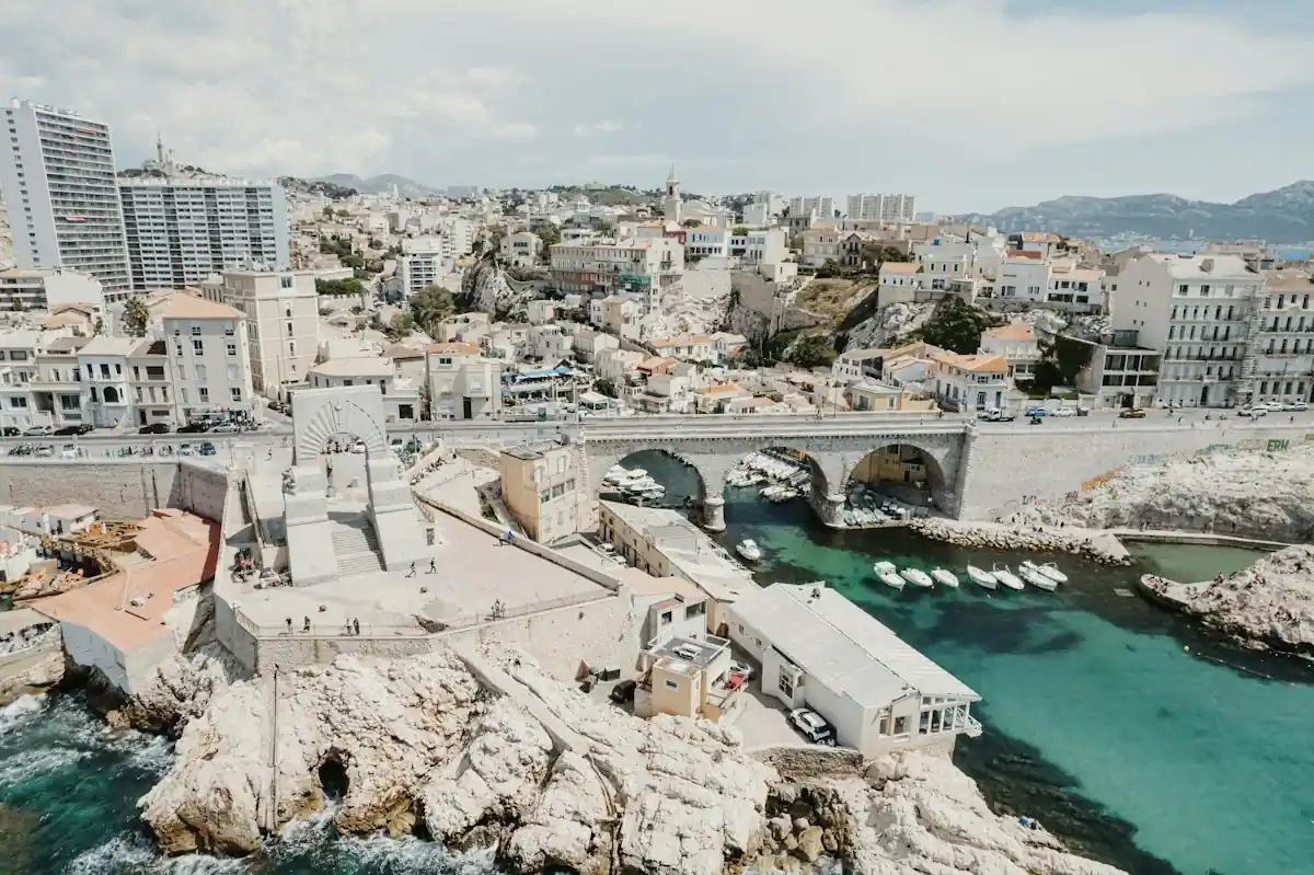 A small fishing harbor under a stone bridge on the rocky Marseille coast.