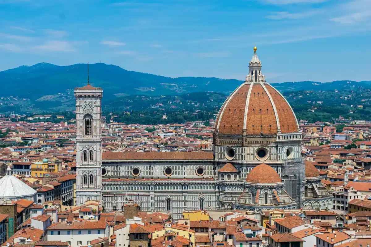 Florence's cathedral dome and bell tower rising above the city's red rooftops, with hills behind.