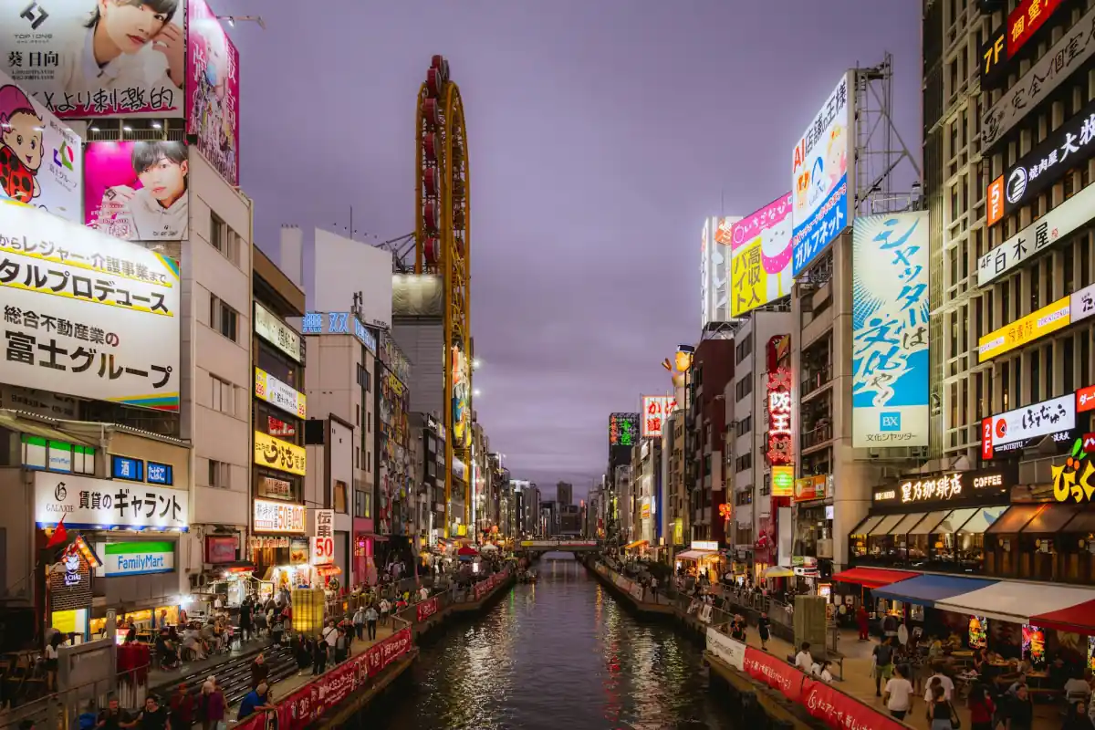 The Dotonbori canal in Osaka at dusk, lined with bright shop signs.